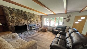 Un salón con pared de piedra, chimenea, sofás de cuero y un trofeo de ciervo colgado.