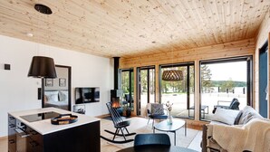 A modern interior with a wooden ceiling, a kitchen area, a dining table, and a seating area with a view of the outdoors. - Saunamäki Resort F - Beachfront (Salo)