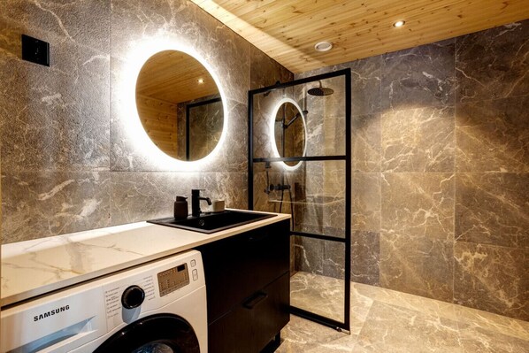 A modern bathroom with a built-in washing machine, a sink with a mirror, and a shower area.