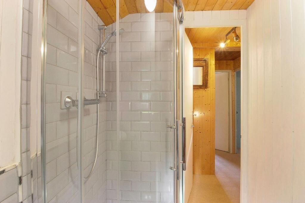 A shower area with white tiled walls and a wooden ceiling.