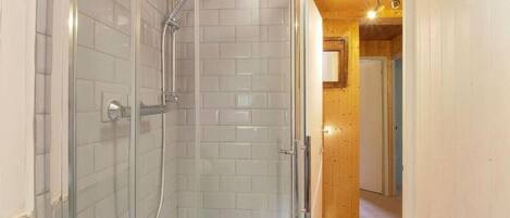 A shower area with white tiled walls and a wooden ceiling.