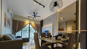 A modern living room with a sofa, dining table, and chairs. There is a ceiling fan and a large window with curtains.