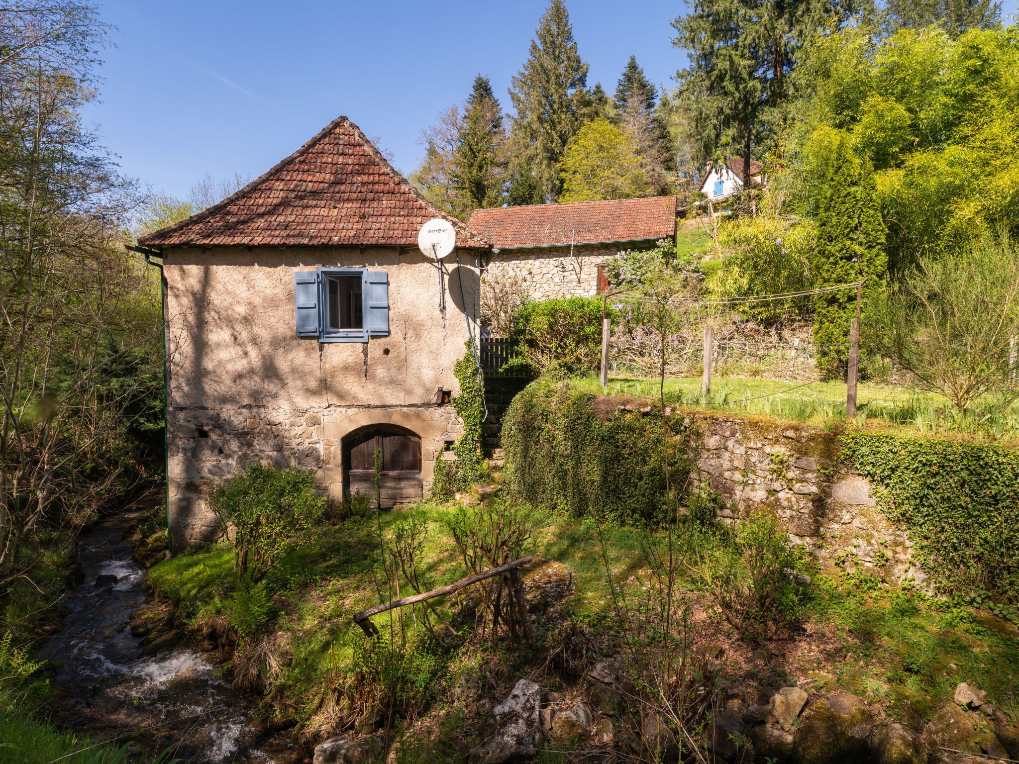 A rustic stone building with a tiled roof, a wooden door, and a satellite dish.