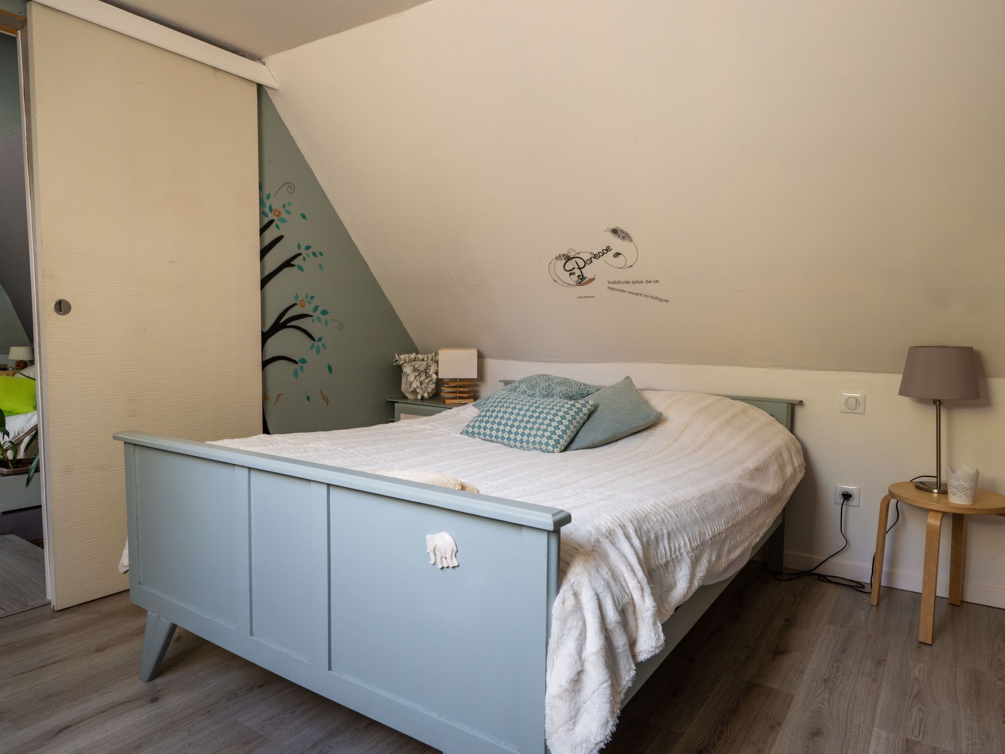Een slaapkamer met een bed, nachtkastje, lamp en een muurdecoratie.