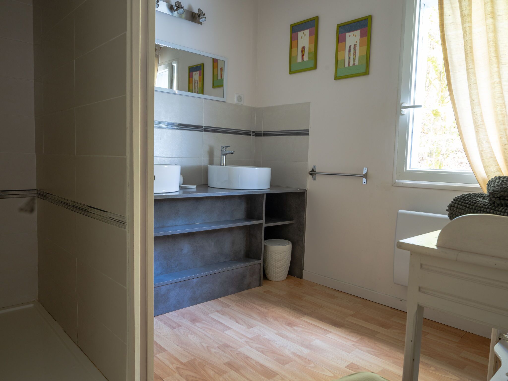 A bathroom with a white sink, mirror, and shelves. There is a window with curtains and a towel rack.