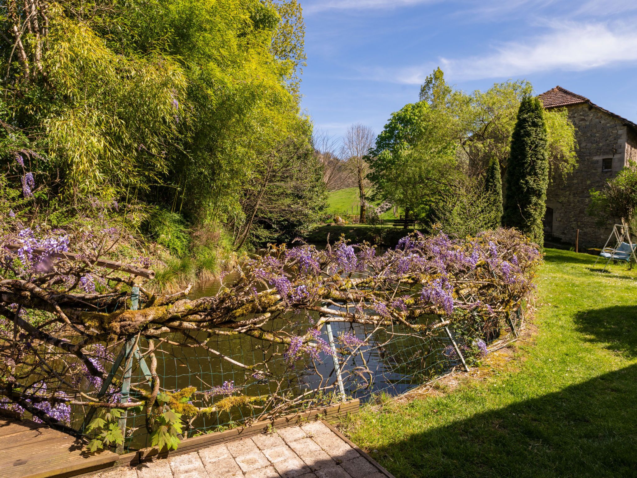 Ein Garten mit einem Steinhaus, einer Holzbrücke über einem Teich und üppiger Bepflanzung.