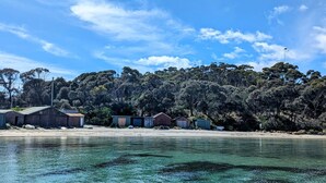 A coastal area with clear water, a sandy beach, and several wooden buildings. - Crow`s Nest - Couples Retreat (Eaglehawk Neck)