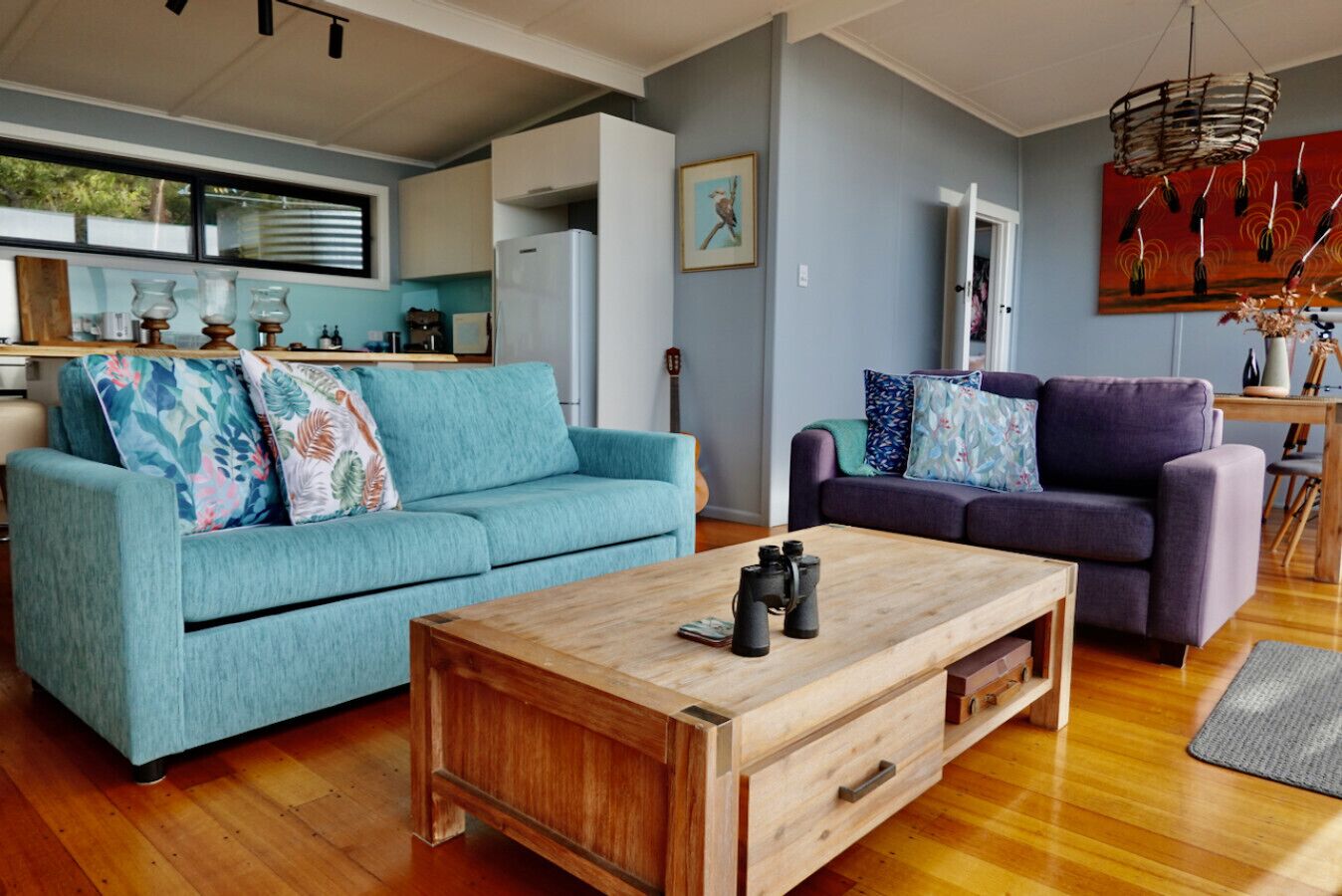 Una sala moderna con un sofá azul turquesa, un sofá púrpura y una mesa de centro de madera.