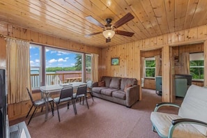 L’intérieur d’une cabane en bois comprend un coin repas, un canapé et un ventilateur de plafond.