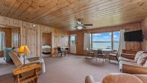 Interieur van een chalet met houten wanden, een plafondventilator, een bank, een tafel en uitzicht op de omgeving.