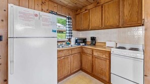 Een functionele keuken met houten kastjes, een witte koelkast, een magnetron, een koffiezetapparaat en een fornuis.