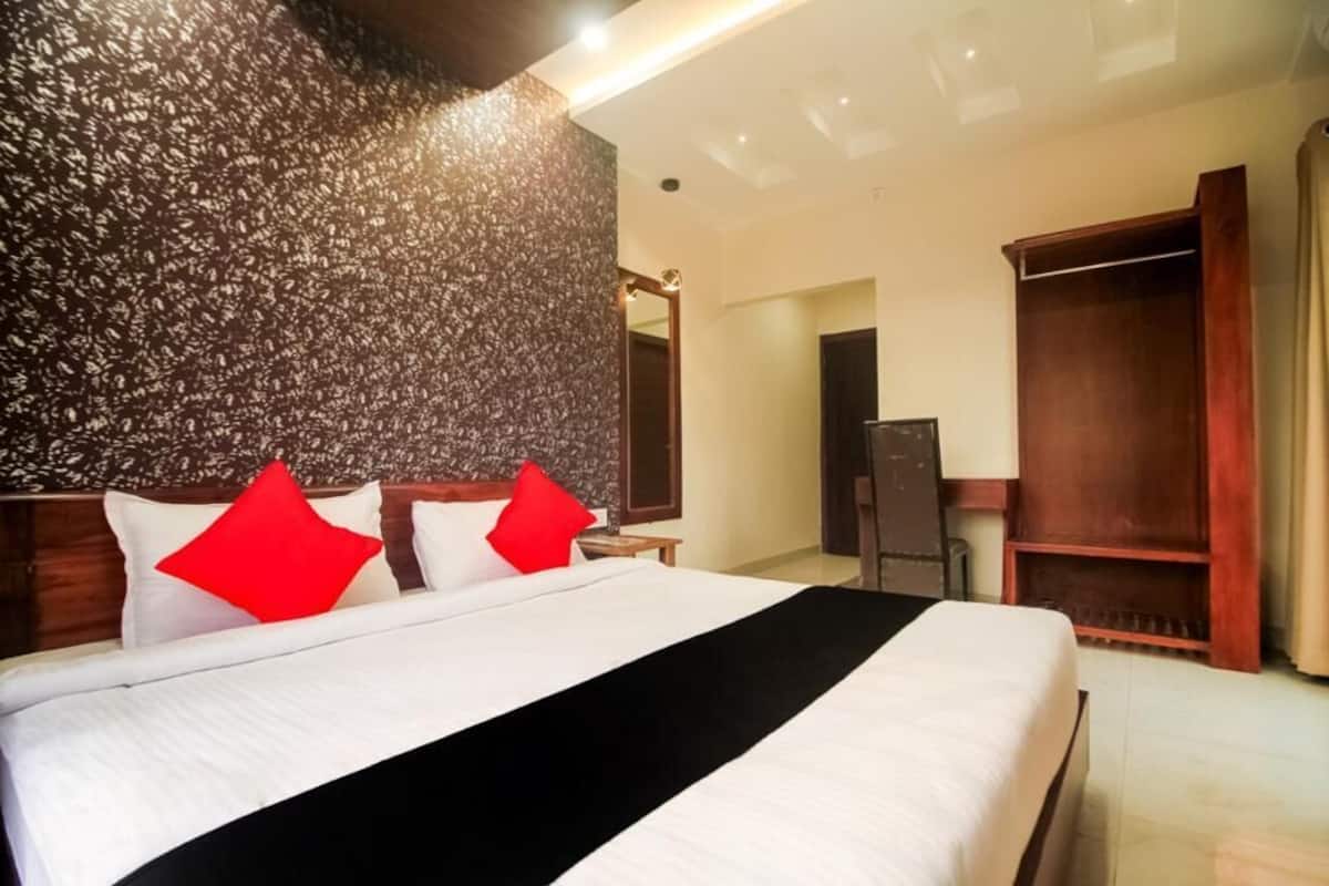 A hotel room with a large bed, a wooden headboard, a dark textured wall, a wardrobe, and a mirror.