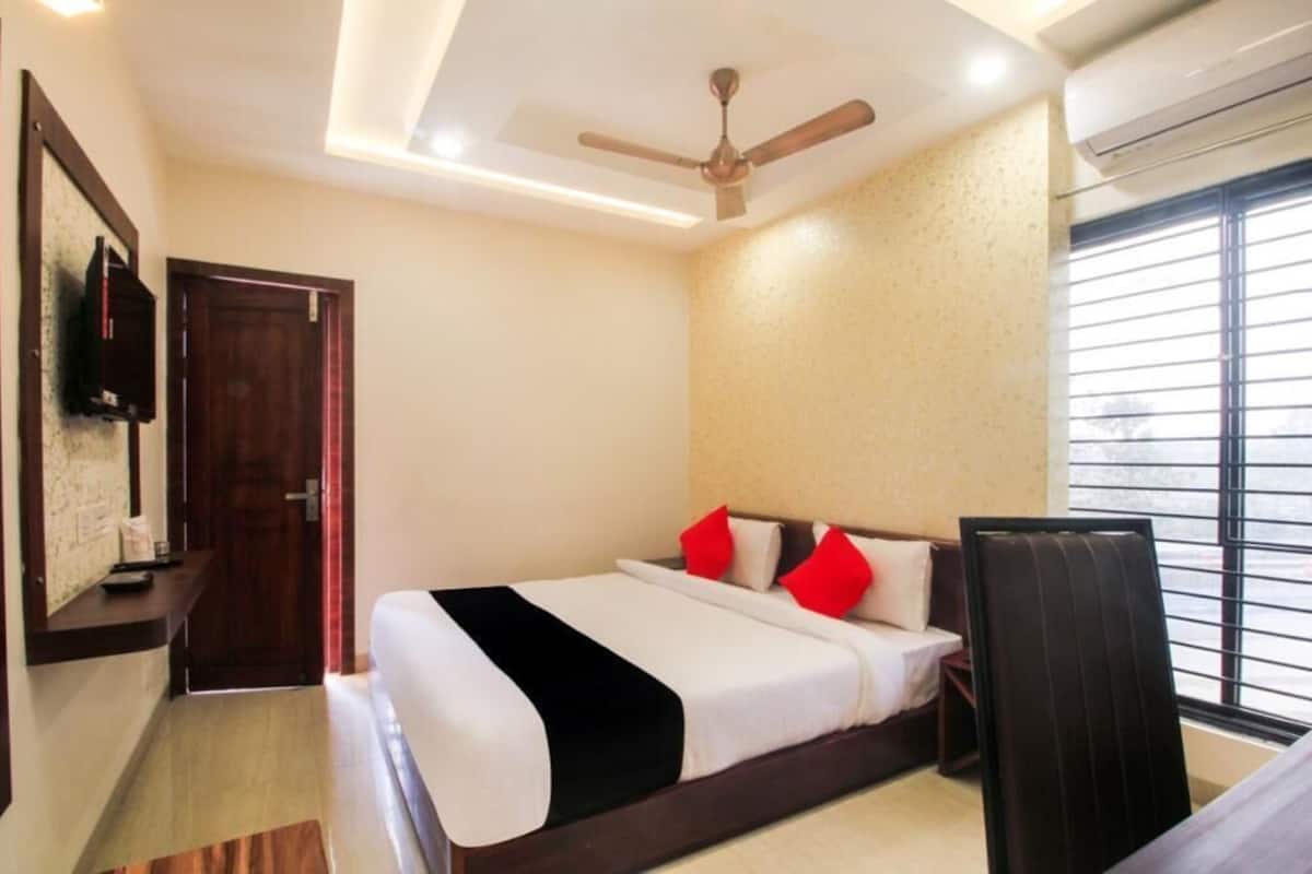 A hotel room with a bed, a ceiling fan, an air conditioning unit, a window with blinds, and a door.