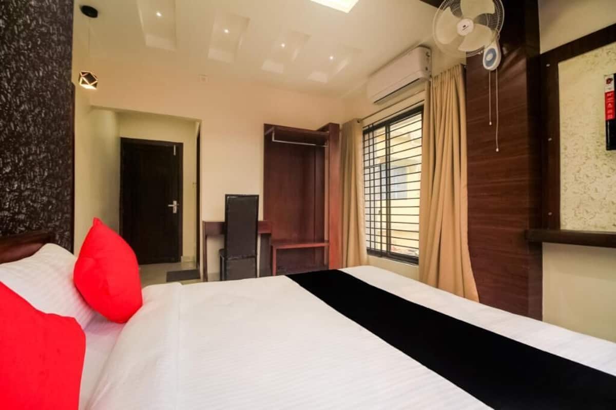 A hotel room with a bed, a ceiling fan, a window with curtains, and a wooden wardrobe.