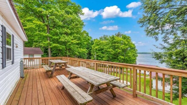Une terrasse en bois avec des tables de pique-nique, donnant sur un lac et entourée d’arbres.