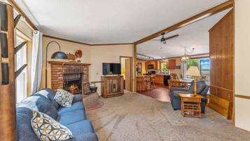 A spacious living room with a fireplace, a sofa set, and a dining area in the background.
