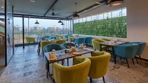 A restaurant with outdoor seating, green chairs, and a view of the city. - Regenta Inn Grand Koramangala  (Bengaluru)