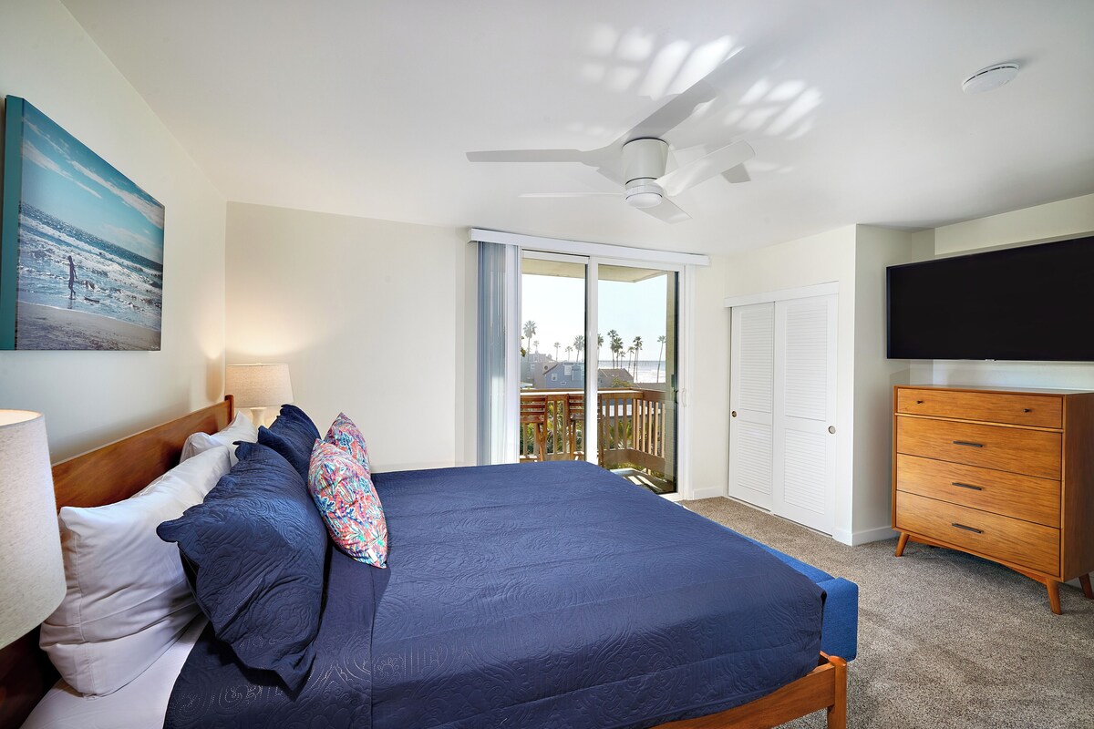 Ein Schlafzimmer mit einem großen Bett, einem Deckenventilator, einem Fernseher und einer Schiebetür zu einem Balkon.