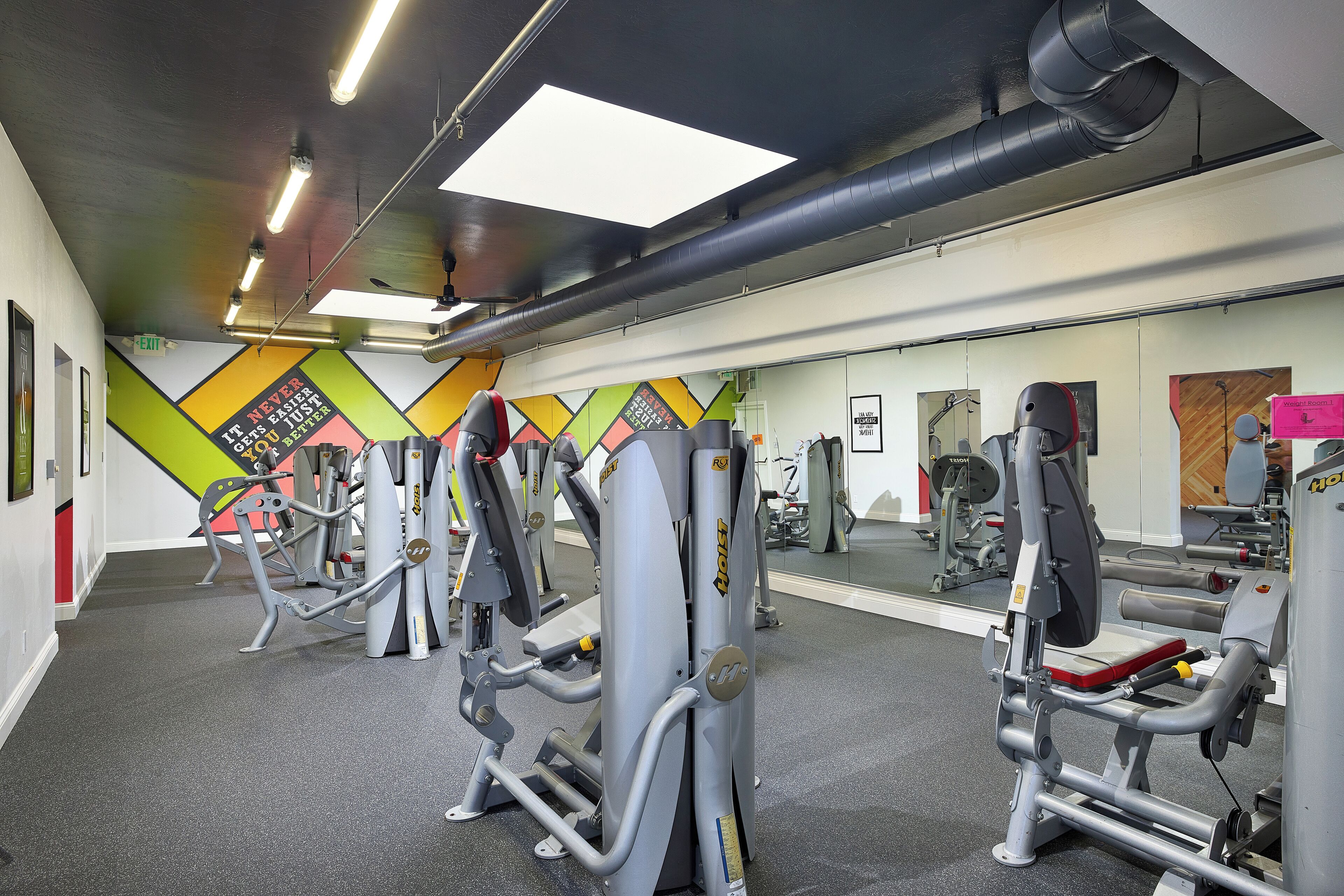 A gym with various exercise machines, a large mirror, and motivational wall art.