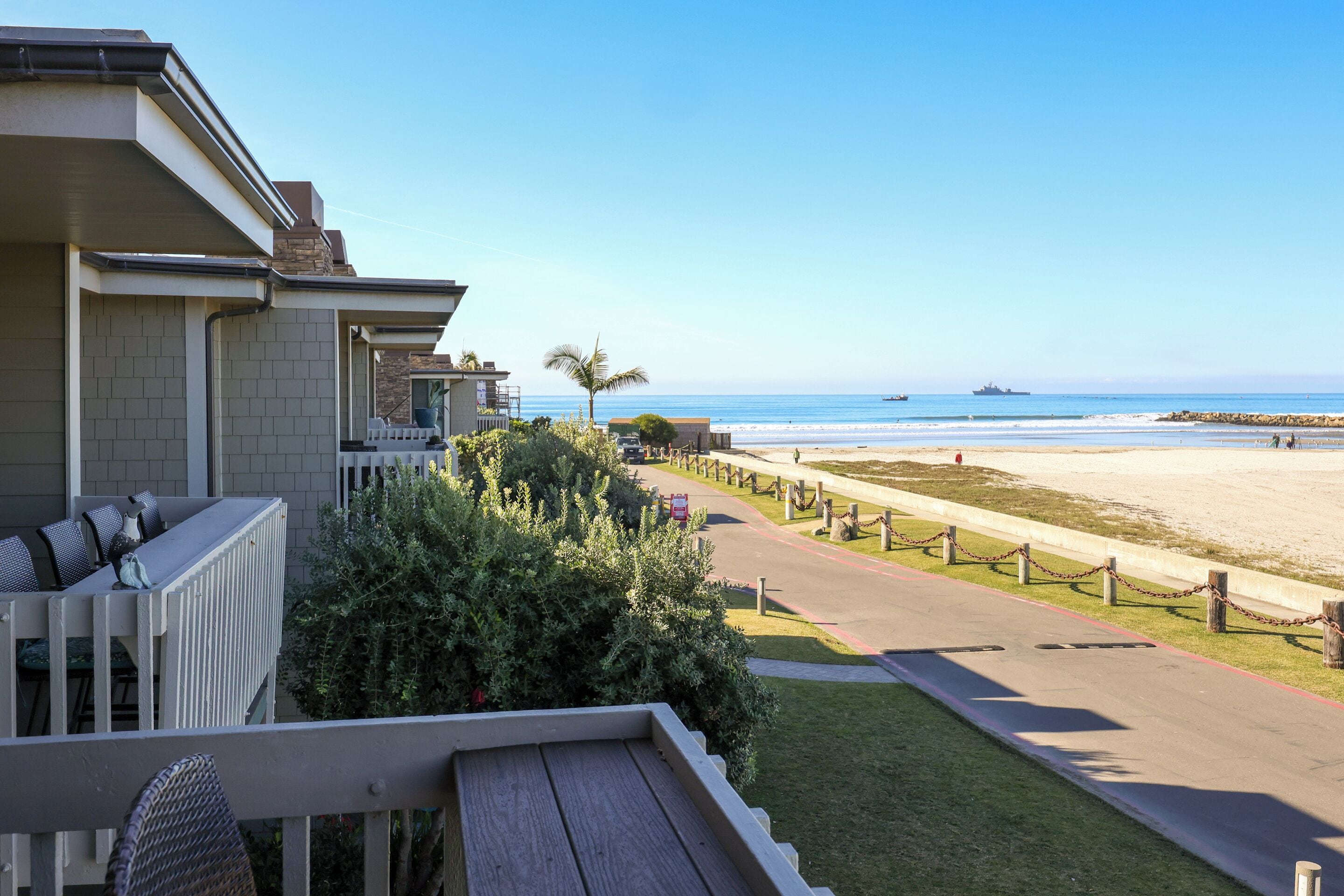Ein Strandgrundstück mit Balkon zum Meerblick, einem gepflasterten Weg und Blick auf den Ozean.