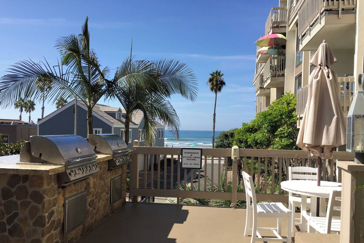 A patio with a barbecue grill, white chairs, and a view of the ocean.