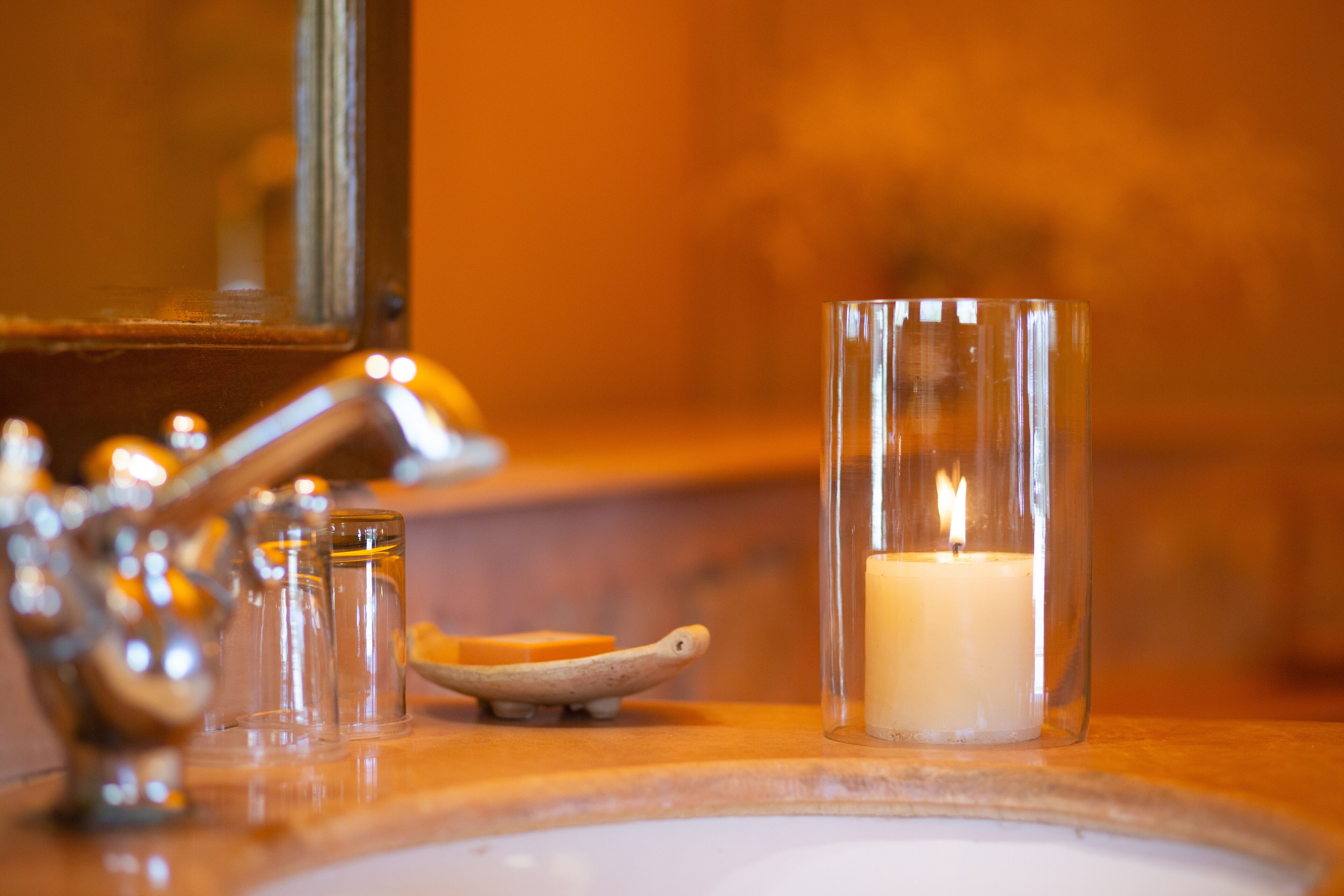 Un lavabo in bagno con una candela accesa in un portacandele di vetro, un piccolo recipiente e un rubinetto.