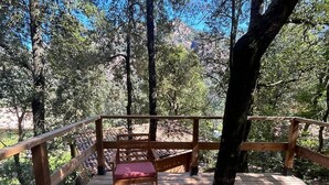 Una terraza de madera con bancos y una mesa, rodeada de árboles.