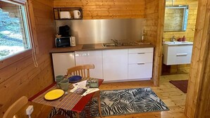 Una cabaña de madera acogedora con kitchenette, un comedor con mesa y sillas, y un baño pequeño visible a través de un vano abierto.