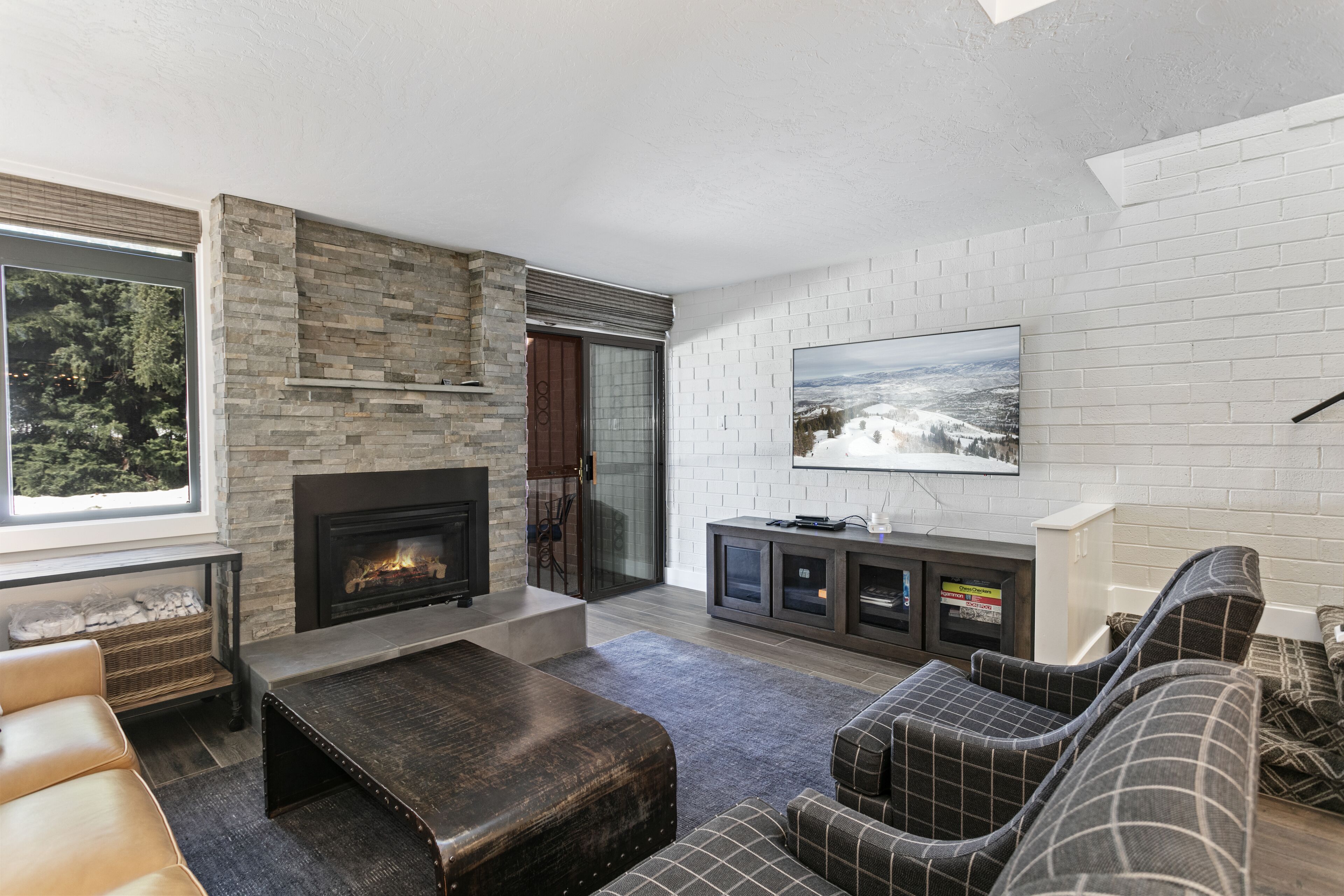 Ein modernes Wohnzimmer mit Kamin, großem Wandfernseher und einer gemütlichen Sitzecke mit Sofa und Sesseln.
