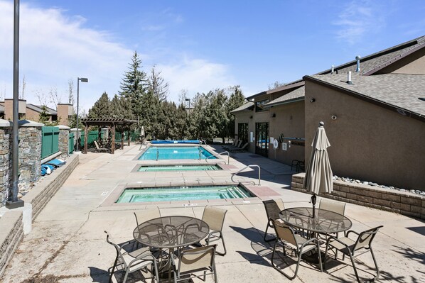 A pool area with multiple swimming pools, outdoor seating, and a building with a sloped roof. - Park Ave by Luxury Mountain Destinations (Park City)