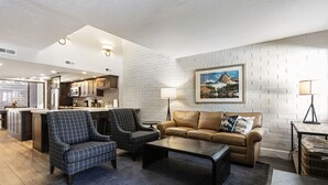 Un salon moderne avec un canapé, deux fauteuils, une table basse et une cuisine en arrière-plan.