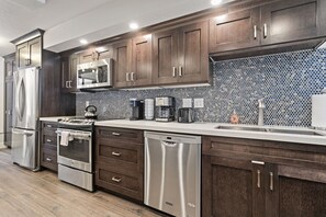 A modern kitchen with stainless steel appliances, dark wooden cabinets, and a tiled backsplash. - Park Ave by Luxury Mountain Destinations (Park City)