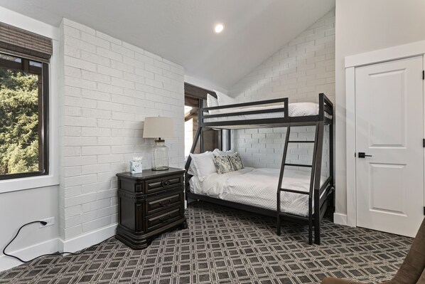A bunk bed room with white brick walls, a dresser, a lamp, and a patterned carpet. - Park Ave by Luxury Mountain Destinations (Park City)