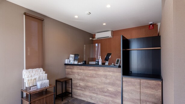 A reception area with a wooden counter, a small seating area, and a trash bin. - HOTEL R9 The Yard Sakuragawa (Sakuragawa)