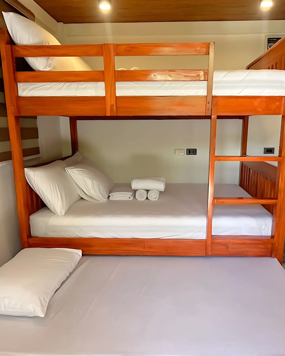 Habitación con literas de madera, ropa de cama blanca y una mesita con toallas.