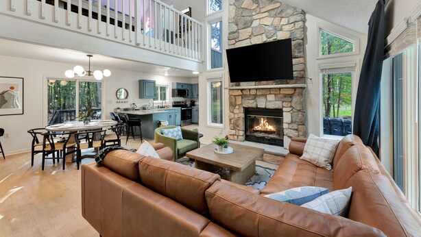 A spacious living area with a stone fireplace, a high ceiling, and a balcony.