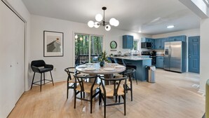 A modern kitchen with blue cabinets, a stainless steel refrigerator, and a dining area with a round table and chairs.
