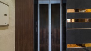 A modern elevator with a glass door, a wooden panel on the left, and a dark wall with reflective panels on the right. - Treebo Taj Dream Agra (Agra)