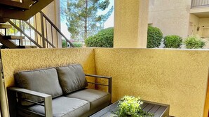 A modern outdoor living area with a gray sofa, a wooden coffee table with a floral arrangement, and a metal staircase leading to an upper level. - ++PRIME LOCATION++ Cozy Condo in Tucson Catalina Foothills Area (Tucson)
