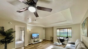 A living room with a ceiling fan, a TV on a white entertainment unit, a gray sofa, a coffee table, and a potted plant. - ++PRIME LOCATION++ Cozy Condo in Tucson Catalina Foothills Area (Tucson)