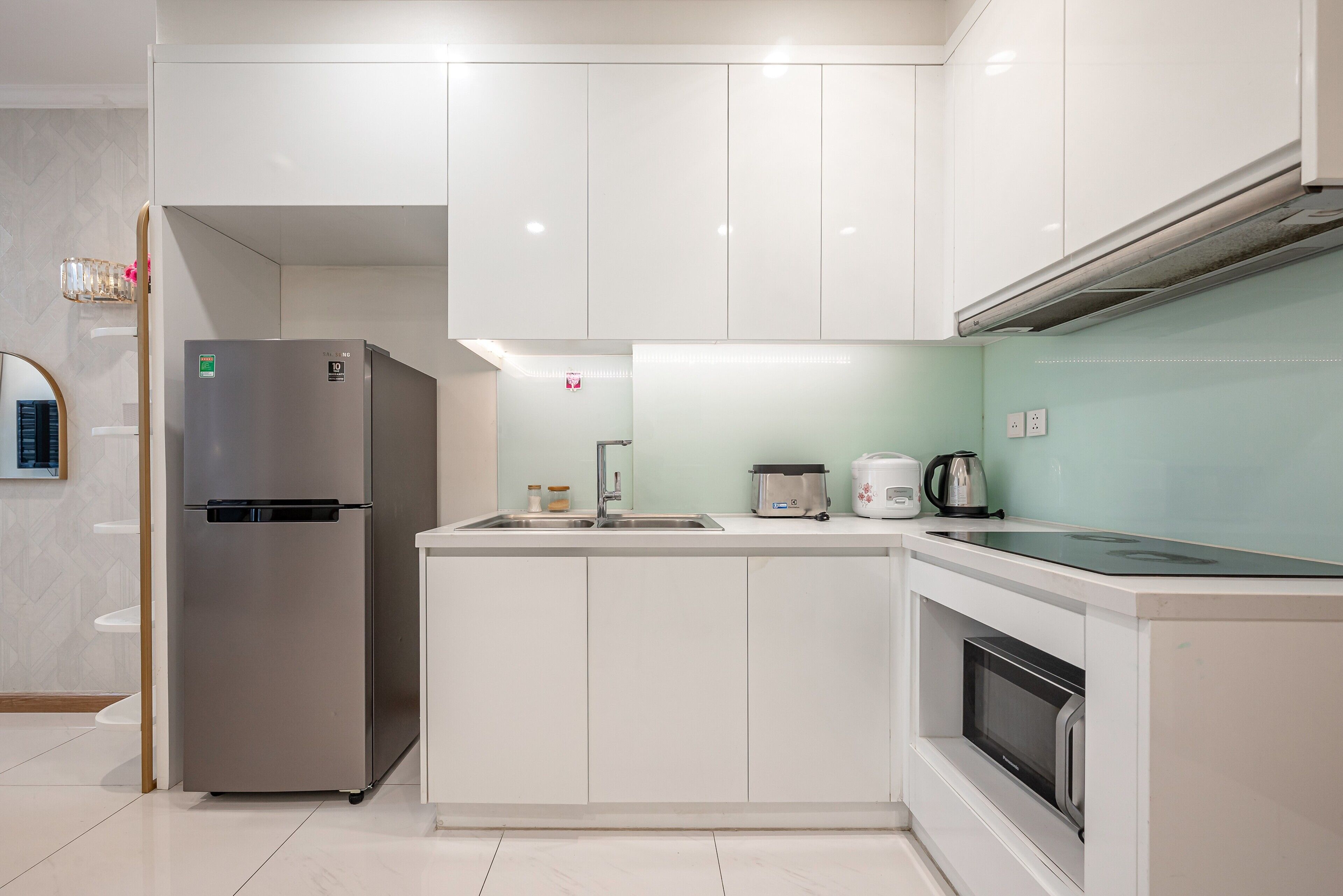 A modern kitchen with white cabinets, a stainless steel refrigerator, a microwave, and a kettle on the countertop.