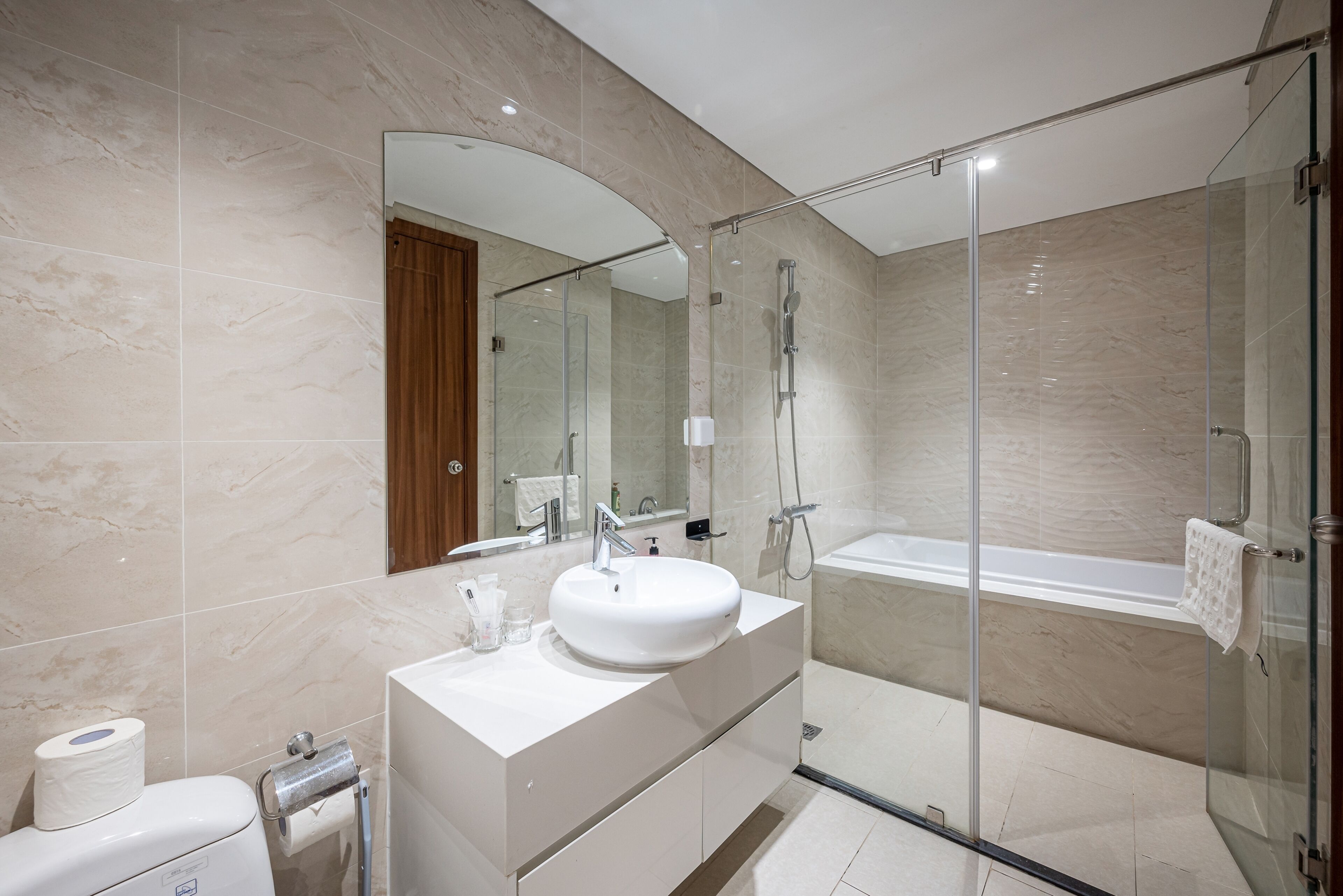 Un baño moderno con ducha de vidrio, lavamanos blanco y un espejo grande.