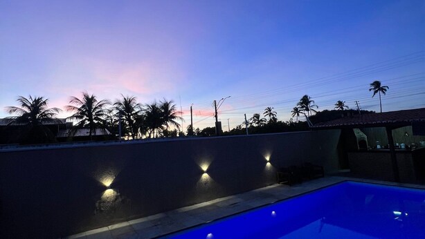 A swimming pool with a curved edge, surrounded by a low wall with three wall-mounted lights. - Pousada Summer Kite Cumbuco (Caucaia)