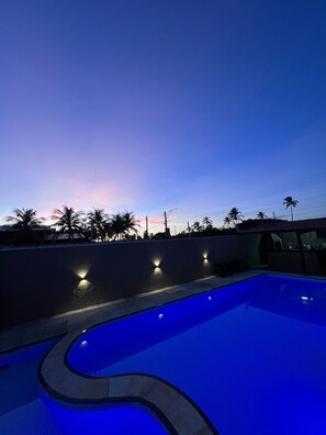 A swimming pool with a curved edge, surrounded by a low wall with three wall-mounted lights. - Pousada Summer Kite Cumbuco (Caucaia)