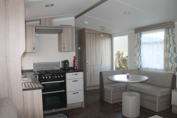 A compact kitchen with a stove, oven, and cabinets, a small round table, and a bench with a cushion.