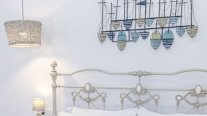 Una cama bien hecha con almohadas a rayas, una mesita de noche con lámpara y una decoración de barcos a vela.