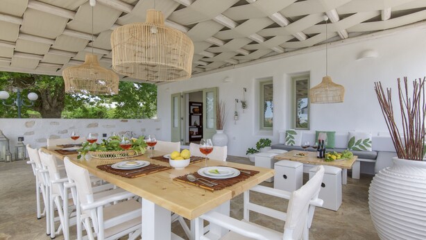 Comedor con una mesa de madera dispuesta para cuatro personas, sillas blancas y lámparas colgantes de mimbre.
