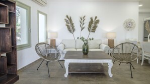 Una sala de estar con un sofá blanco, dos sillones de mimbre, una mesa de centro y un jarrón decorativo.