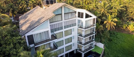 A multi-story building with balconies, surrounded by lush greenery and palm trees.