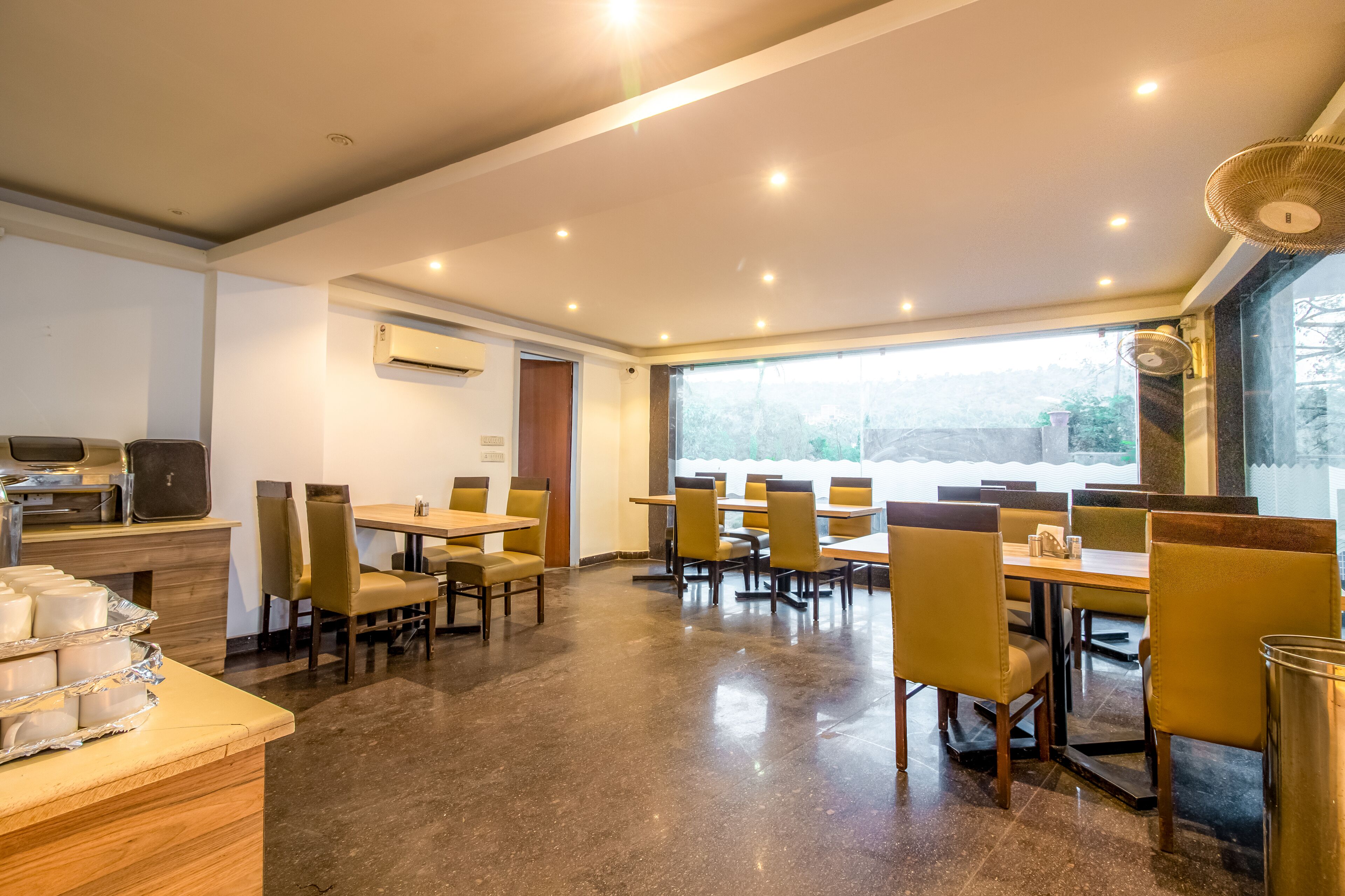 Un espace repas moderne, doté de tables et de chaises, d’un comptoir de service et d’une grande fenêtre offrant une vue sur l’extérieur.